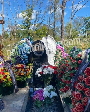 Двойной памятник из чёрного гранита с округлым верхом, оформленный цветами