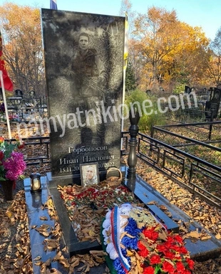 Вертикальный памятник из чёрного гранита с гравированным портретом, ограда и венки