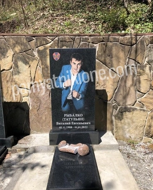 Памятник из чёрного гранита с цветным портретом в полный рост у каменной стены