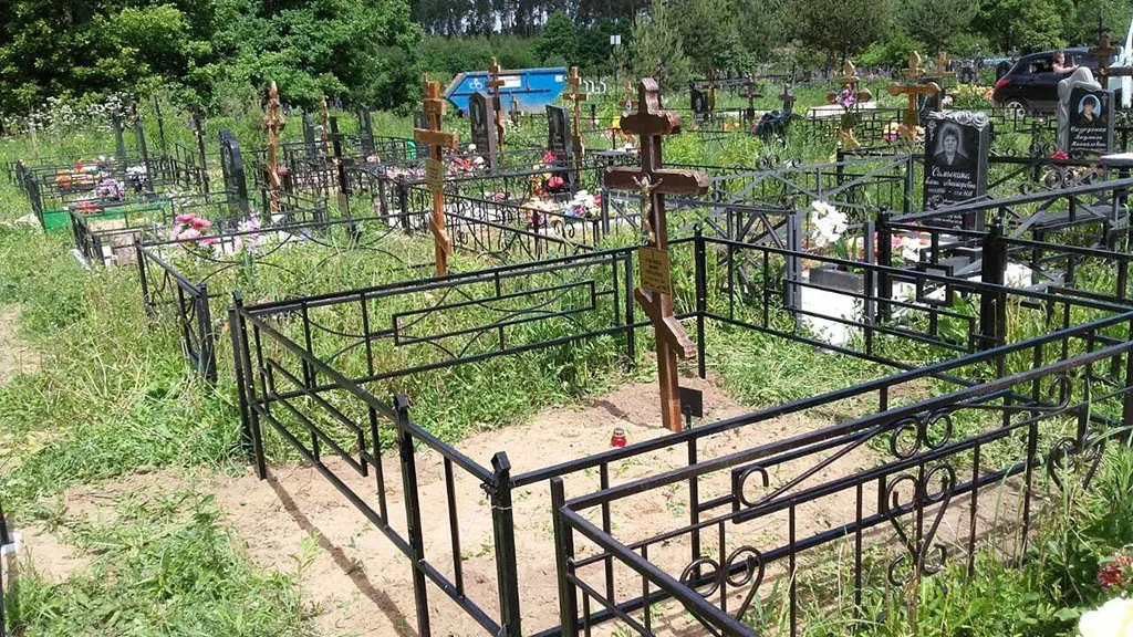 Участок захоронения с деревянным крестом и оградой на сельском кладбище