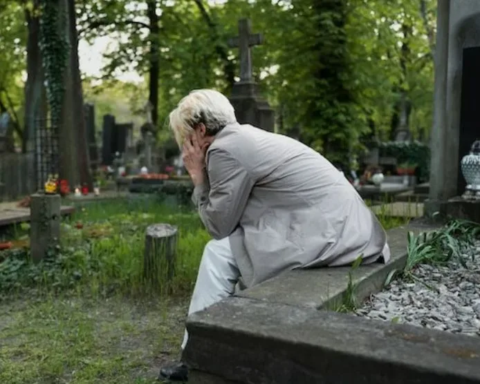 Мужчина горюет, сидя у надгробия на кладбище