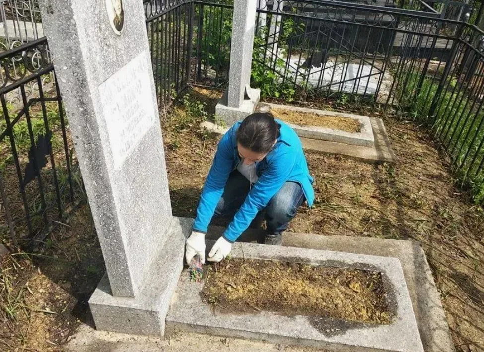 Женщина ухаживает за могилой и убирает сухую траву у памятника